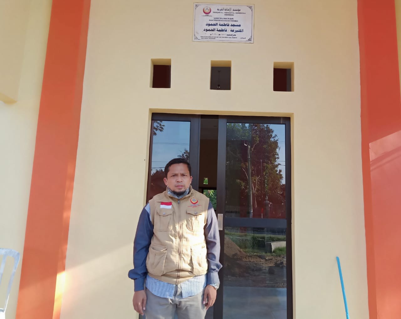 A participant stands at the mosque entrance beneath the programme plaque.