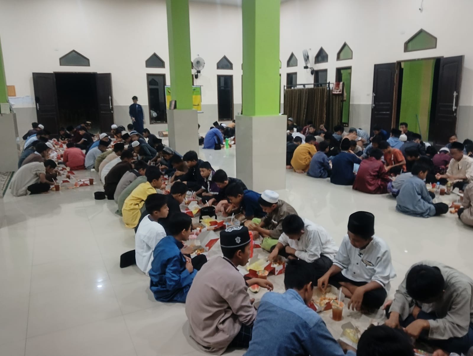 Participants sit in rows sharing a meal inside the mosque.