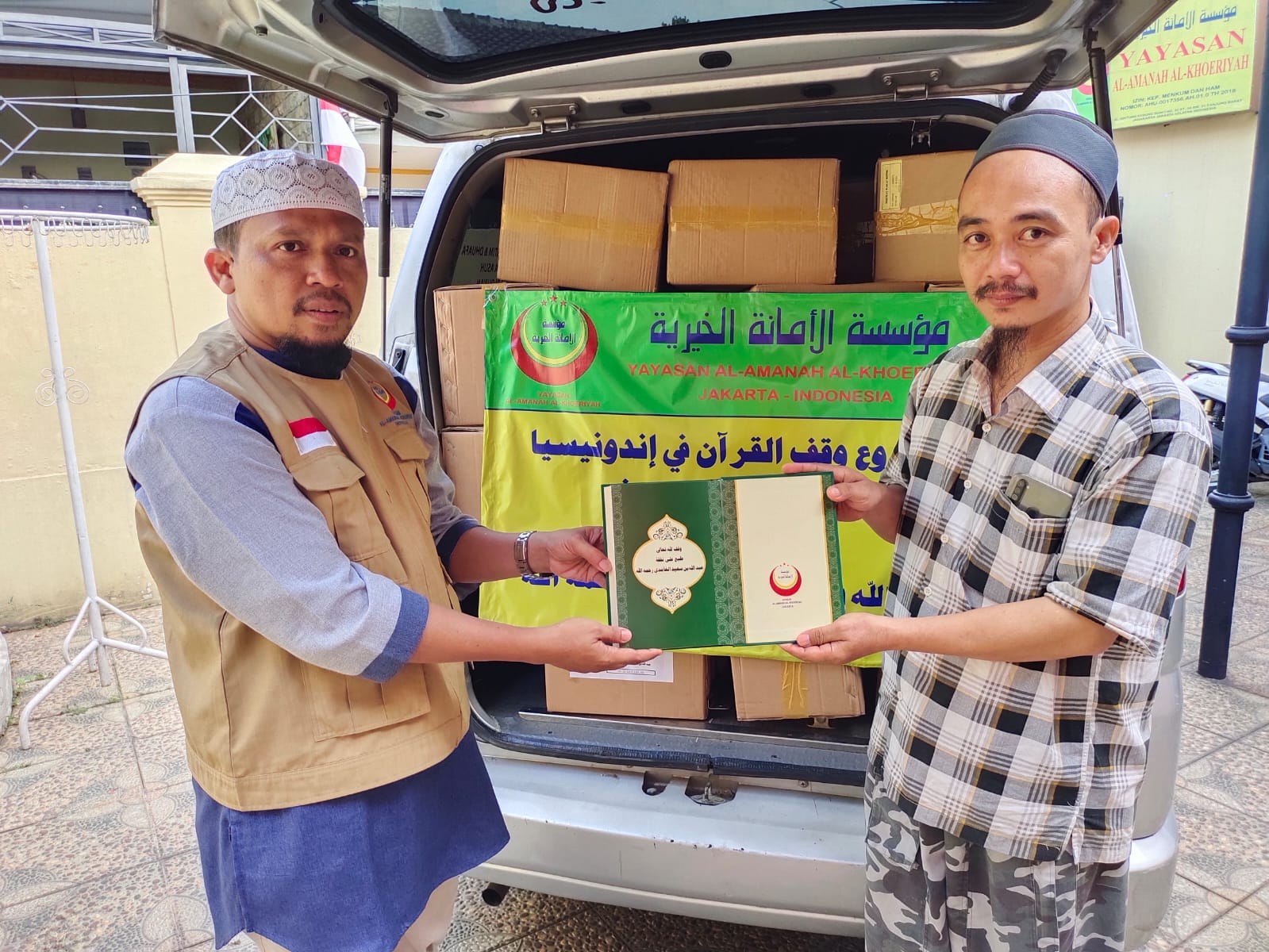 رجلان يعرضان مصحفا مفتوحا أمام الصناديق والسيارة