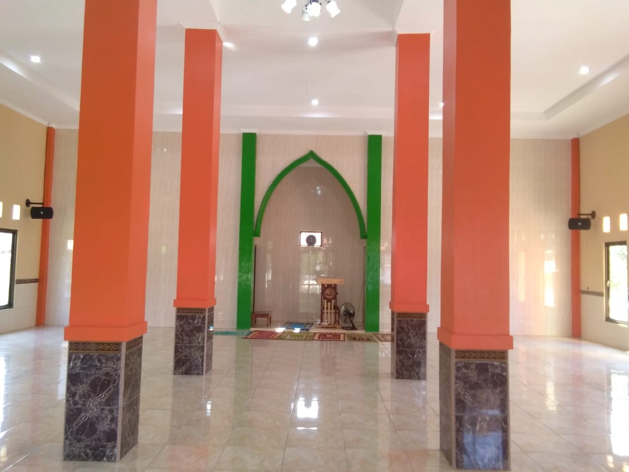 Mosque prayer hall with pillars, tiled floor and windows.
