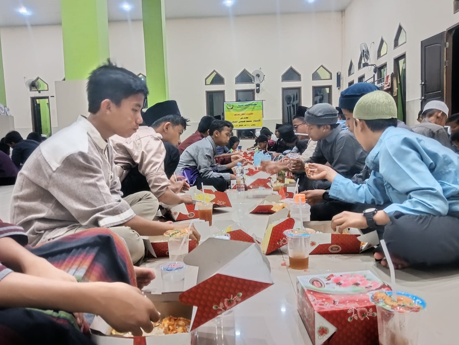 Participants sit in rows sharing a meal inside the mosque.