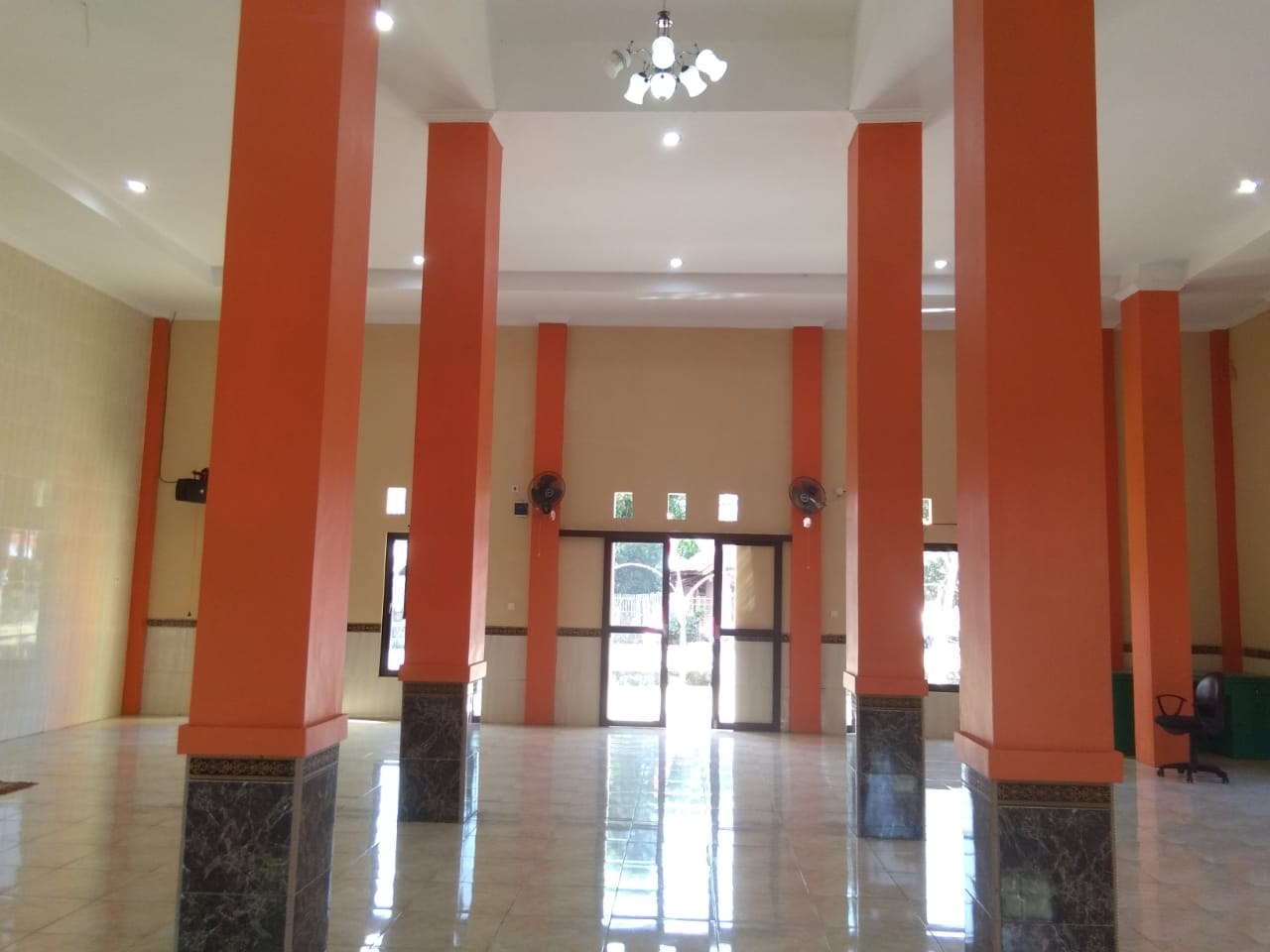 Mosque prayer hall with pillars, tiled floor and windows.