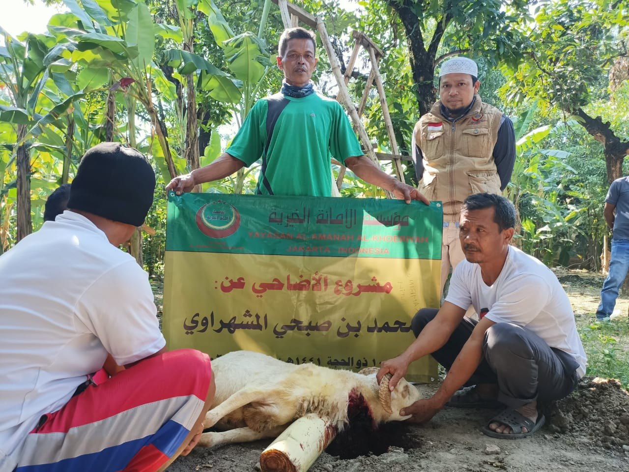 Participants pose with livestock beside the Qurban programme banner.